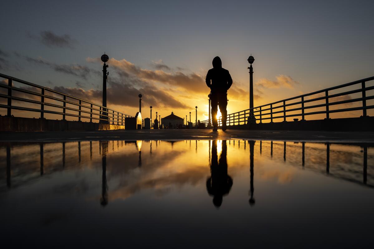 The sunset is reflected in a puddle on the Manhattan Beach Pier while a person is in silhouette