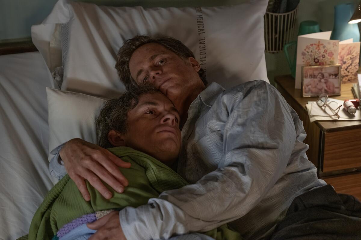 Two men embrace while on a hospital bed