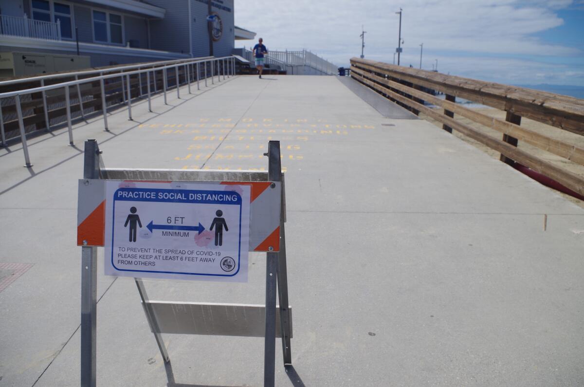Signs remind visitors near the Newport Pier to keep their distance to help prevent spread of the COVID-19 coronavirus. The Newport Pier and the Balboa Pier two miles down the shore were closed Wednesday in an effort to keep people from coming in close contact with one another.