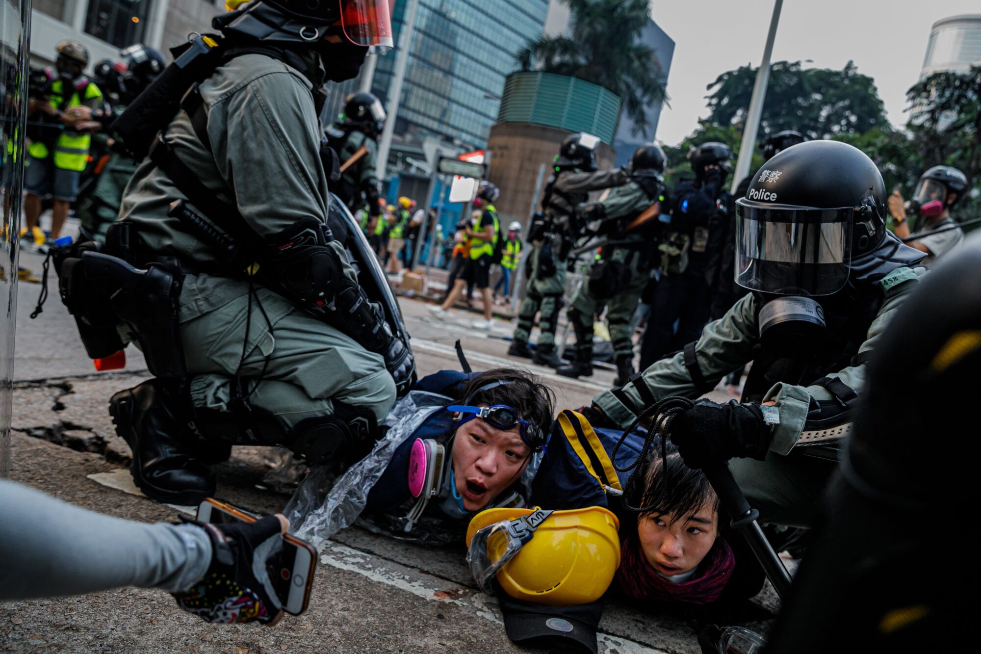 Police officers in riot gear pin down young female protesters on a street in Hong Kong.