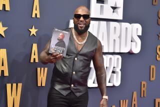 Jeezy is posing with his memoir, "Adversity for Sale," and is smiling while wearing sunglasses and a black vest