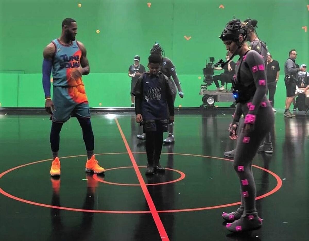Actors and athletes stand on a basketball court with a green screen in the background.