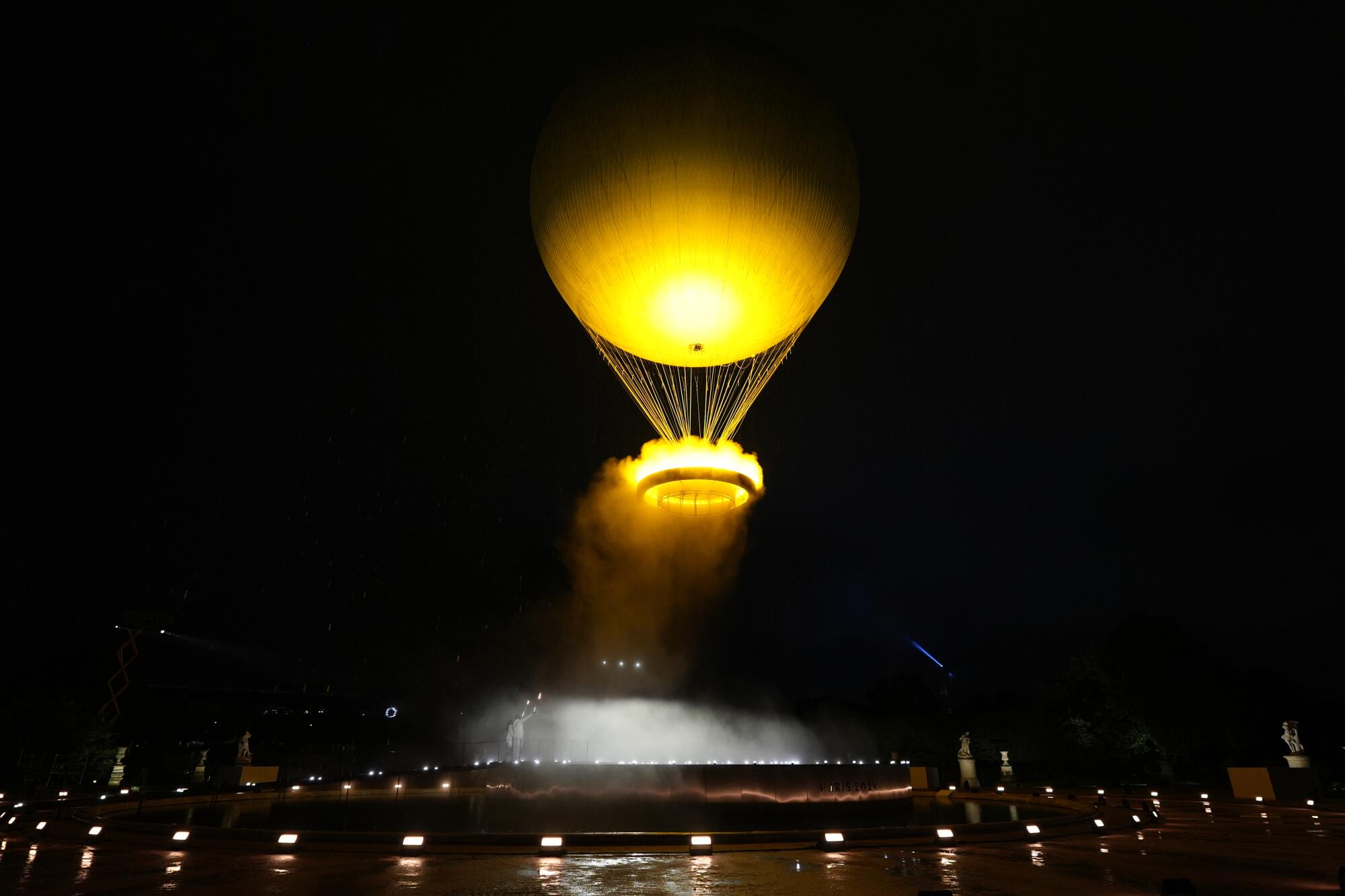 A golden hot-air balloon shaped cauldron rises in the Paris night sky.