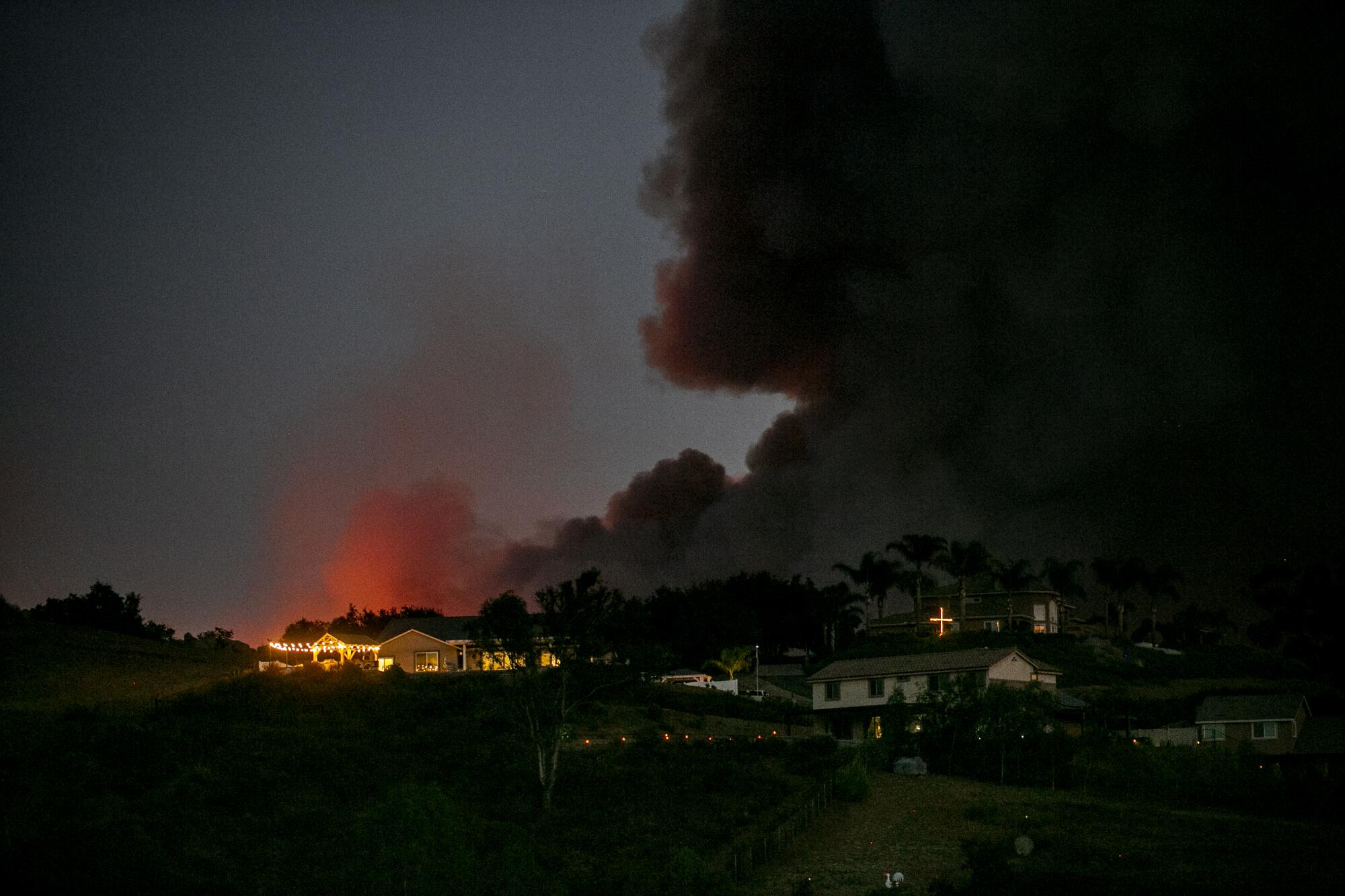 Smoke rises at night behind illuminated buildings.