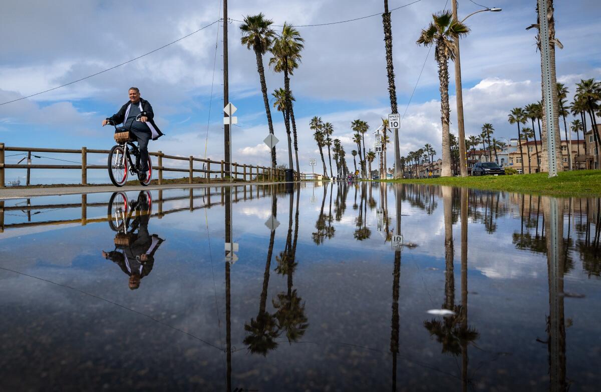 Standing water from recent storms create reflections as a rides by in Huntington Beach