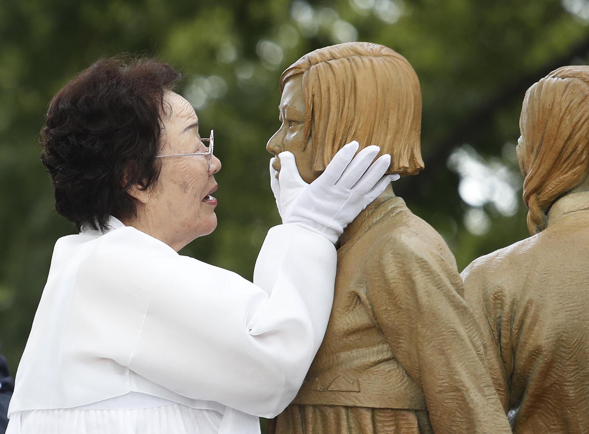 A survivor of sexual slavery embraces the face of a statue with her gloved hands