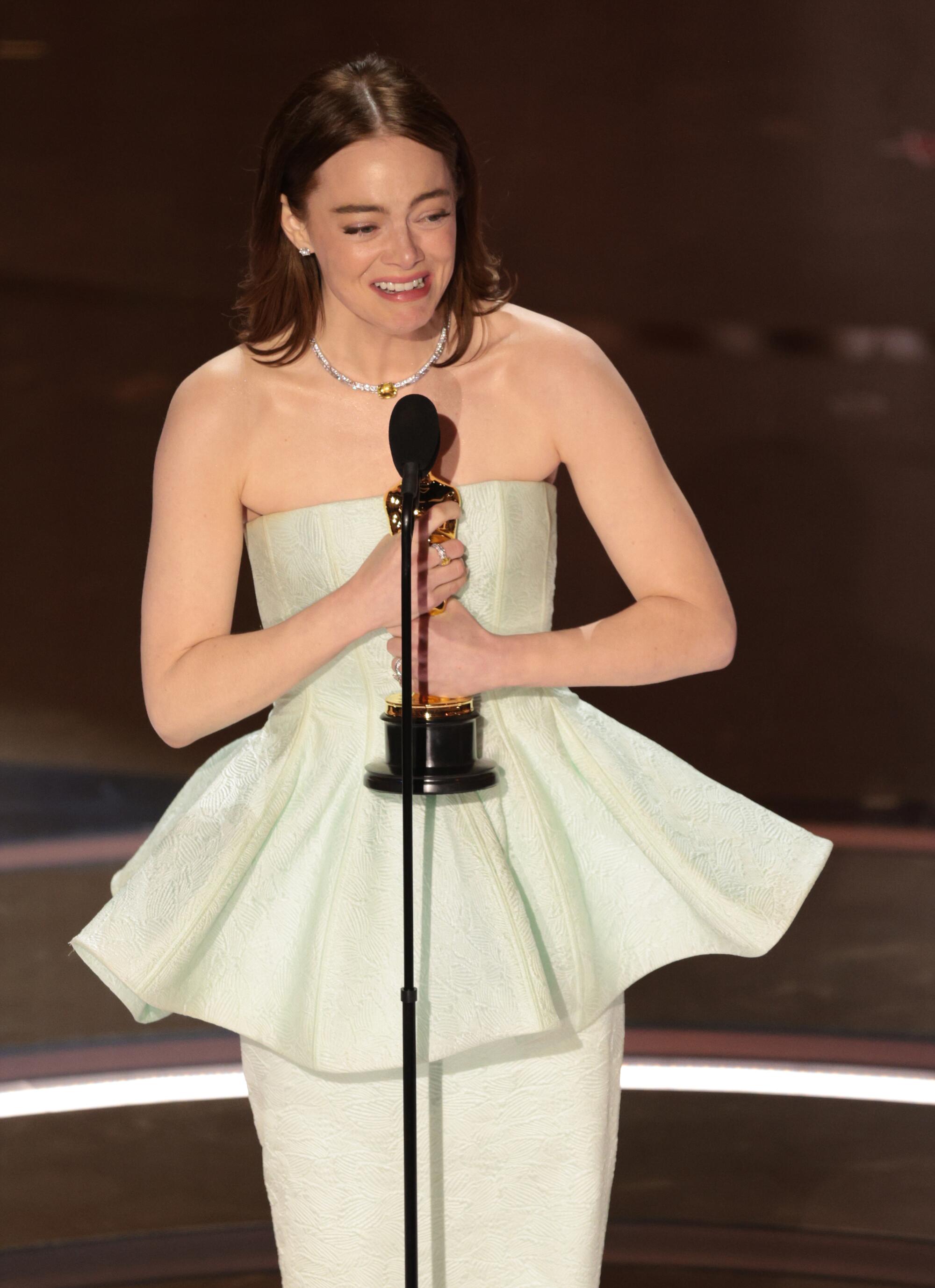 Emma Stone in a white dress clutches an Oscar statuette to her chest.