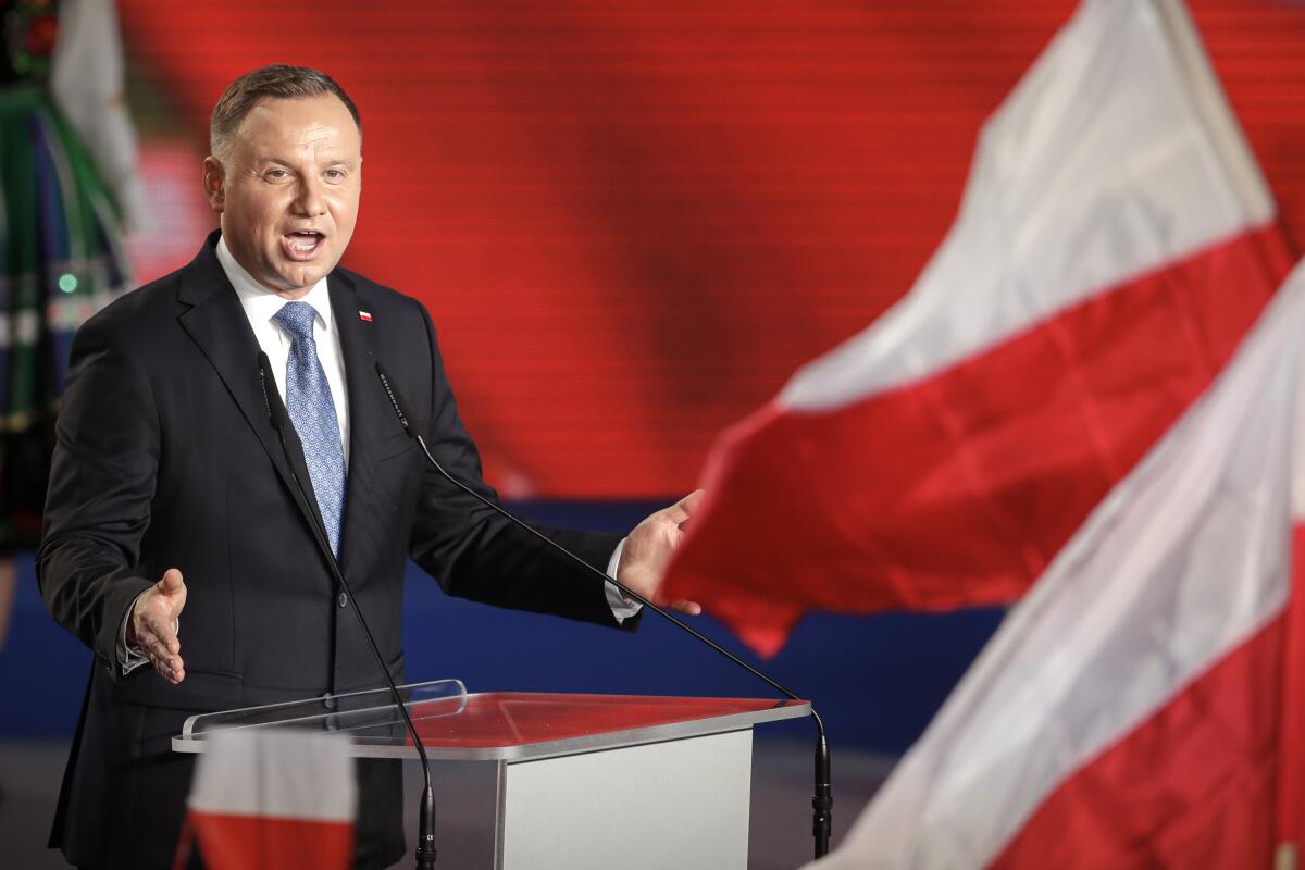 Polish President Andrzej Duda stands at a lectern near Polish flags.