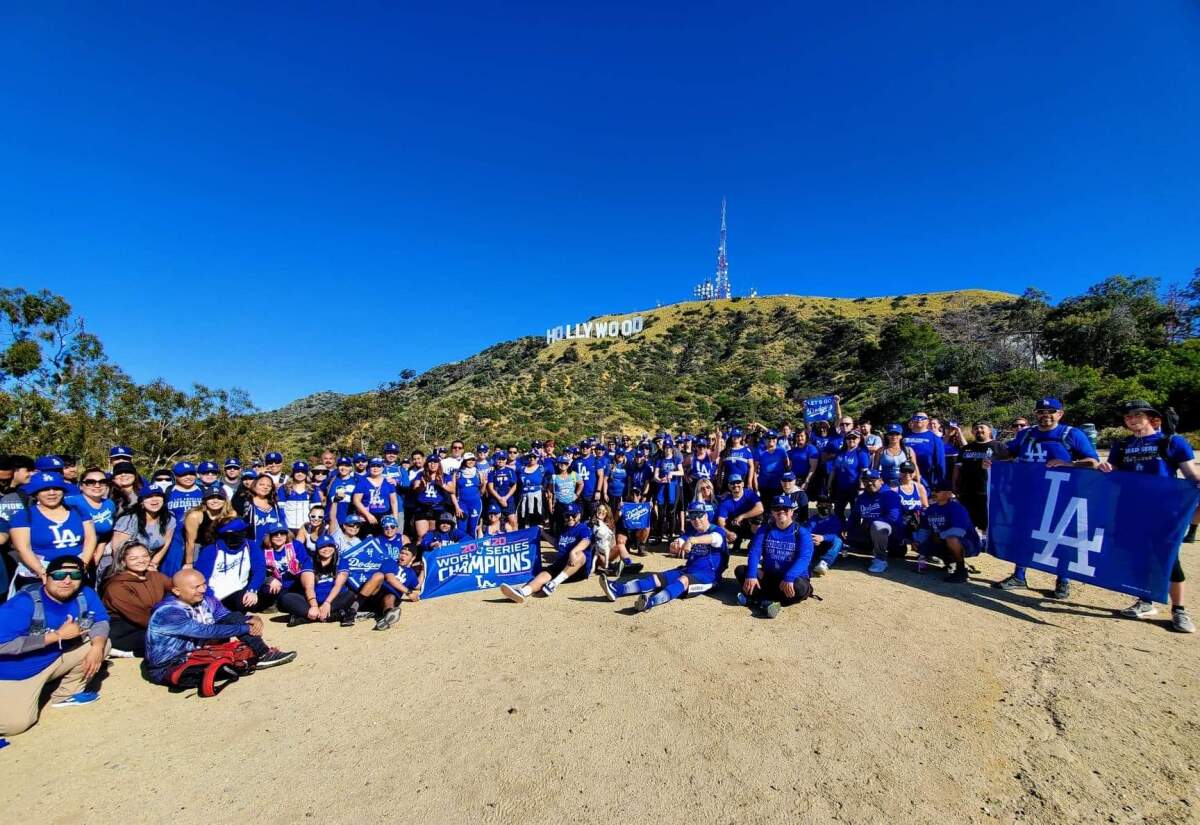 A hiking crew dressed in Dodgers blue poses for a photo beneath the Hollywood sign near Mt. Lee.