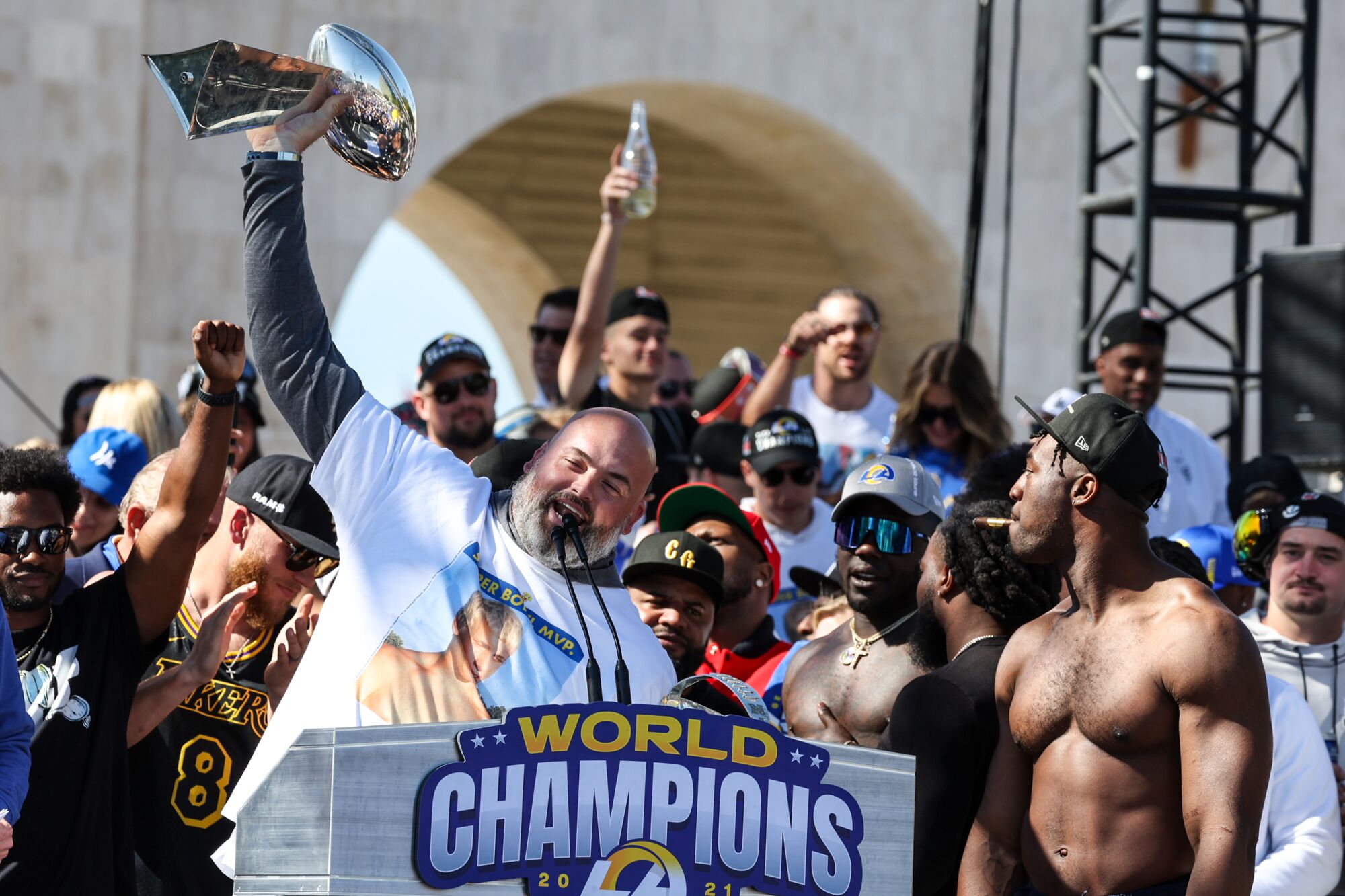Andrew Whitworth hoists the Lombardi Trophy while Rams teammates cheer at the Super Bowl LVI celebration at LA Coliseum.