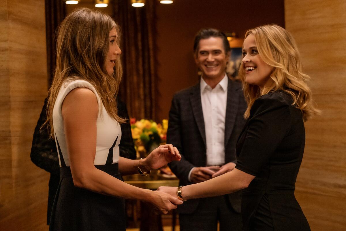 Two women greet each other in an entryway as a man looks on.