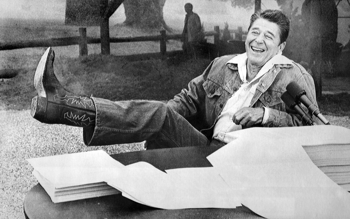 While in Santa Barbara in the summer of 1981, President Reagan shows his boot to reporters who asked if he had any problems with the bubonic plague threat in the area. In front of him lies the economic tax relief bill and budget that he signed while on vacation. (Los Angeles Times)