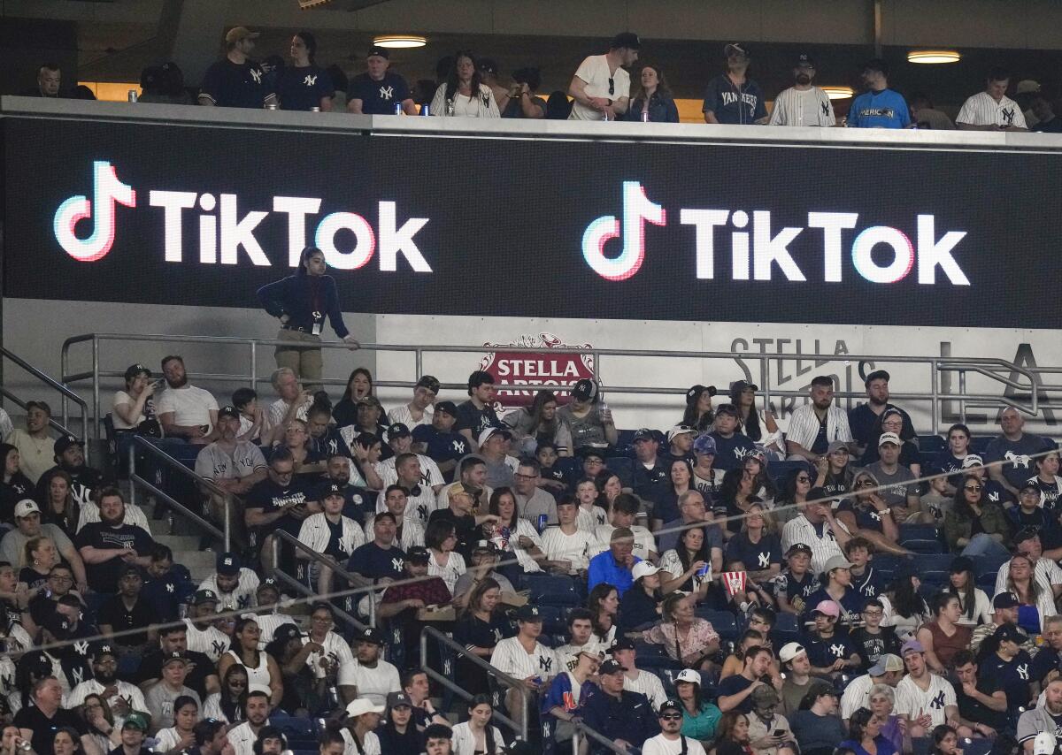 ARCHIVO - Aficionados están sentados bajo un anuncio de TikTok mientras asisten 