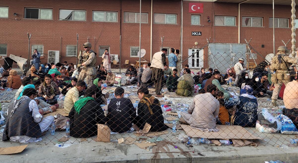 Afghan families stand or sit in a holding area before they board evacuation flights