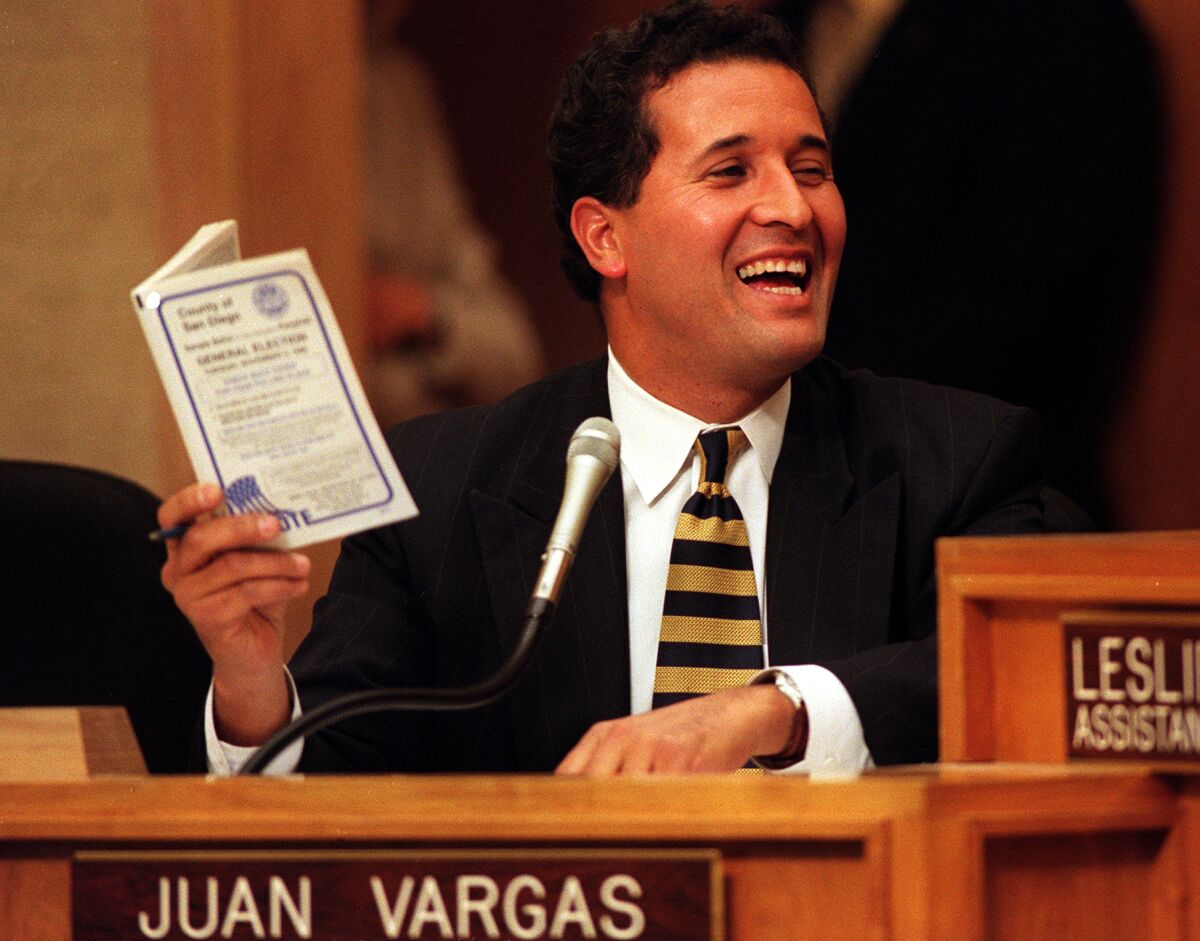 A person sits behind a desk with the nameplate "JUAN VARGAS."