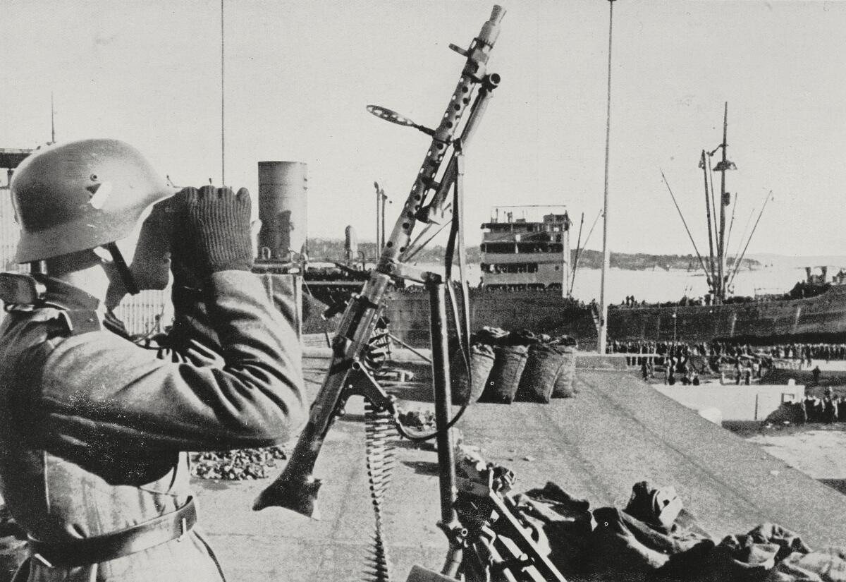 Black-and-white photo of a German machine gunner looking at a port through binoculars.