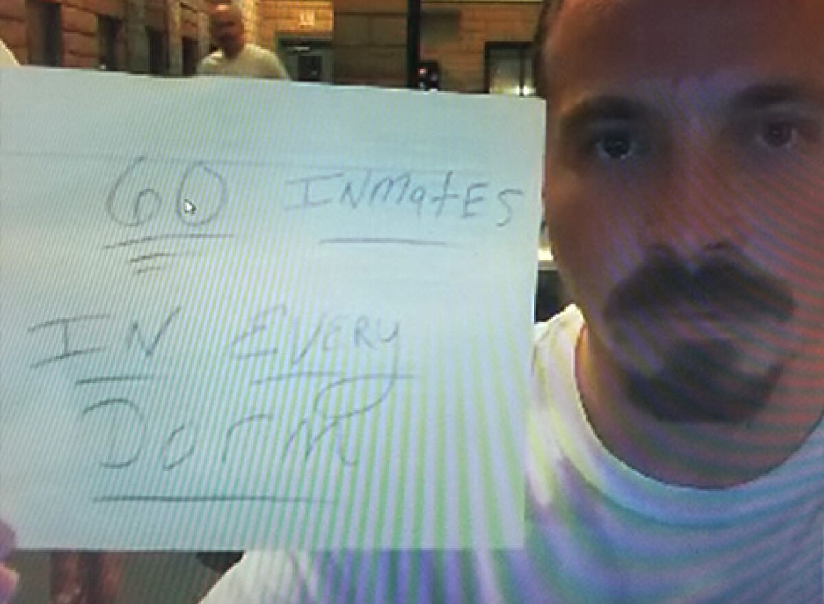 A screen grab from a video call shows Dustin Ehm holding a sign saying "60 Inmates in Every Dorm." He is one of more than 550 men held at the East Mesa Reentry Facility.