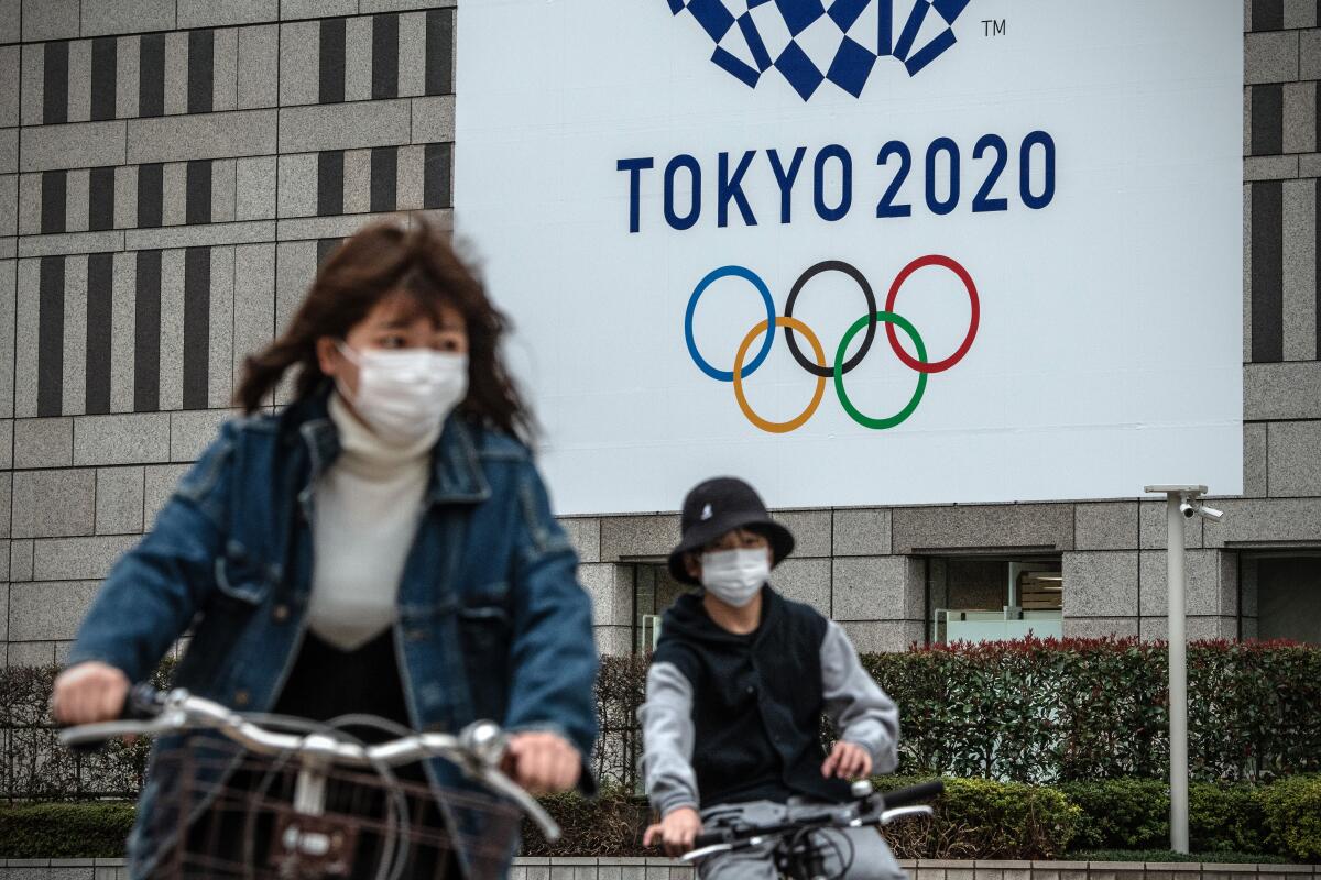 People in Tokyo cycle past a banner for the 2020 Summer Olympics on Friday.