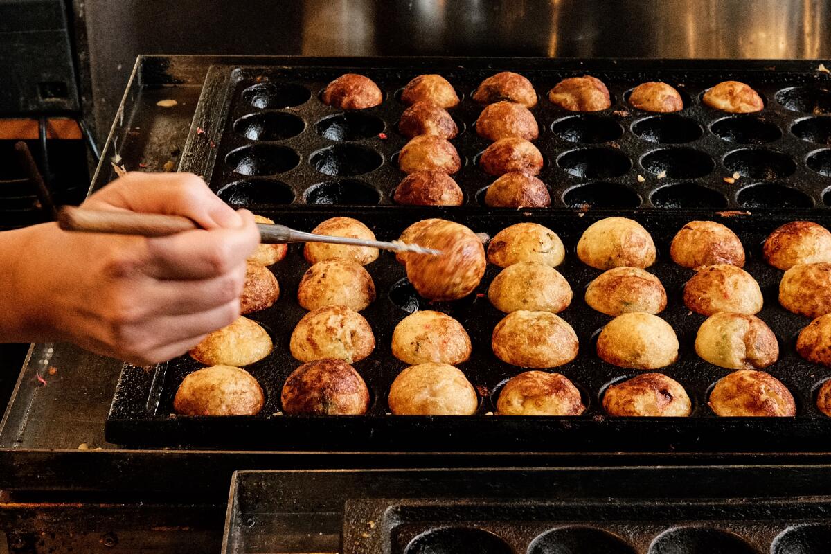 A hand flips takoyaki in a large black griddle at Little Tokyo's Takoyaki Tanota