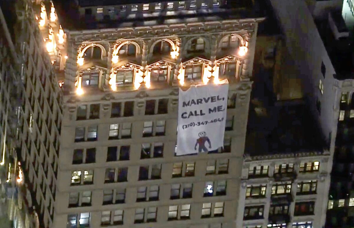 A large banner saying 'Marvel, call me' is displayed on the side of a downtown Los Angeles building.