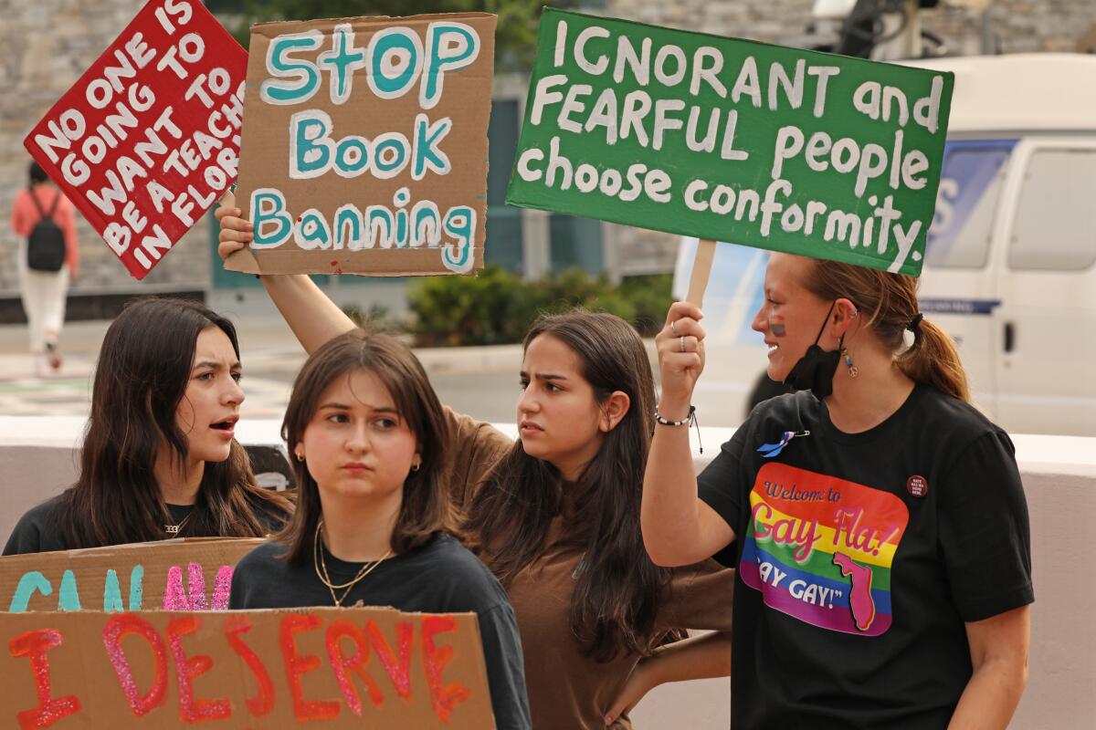 Personas sostienen carteles que prohíben los libros en una reunión de la junta escolar en Florida.