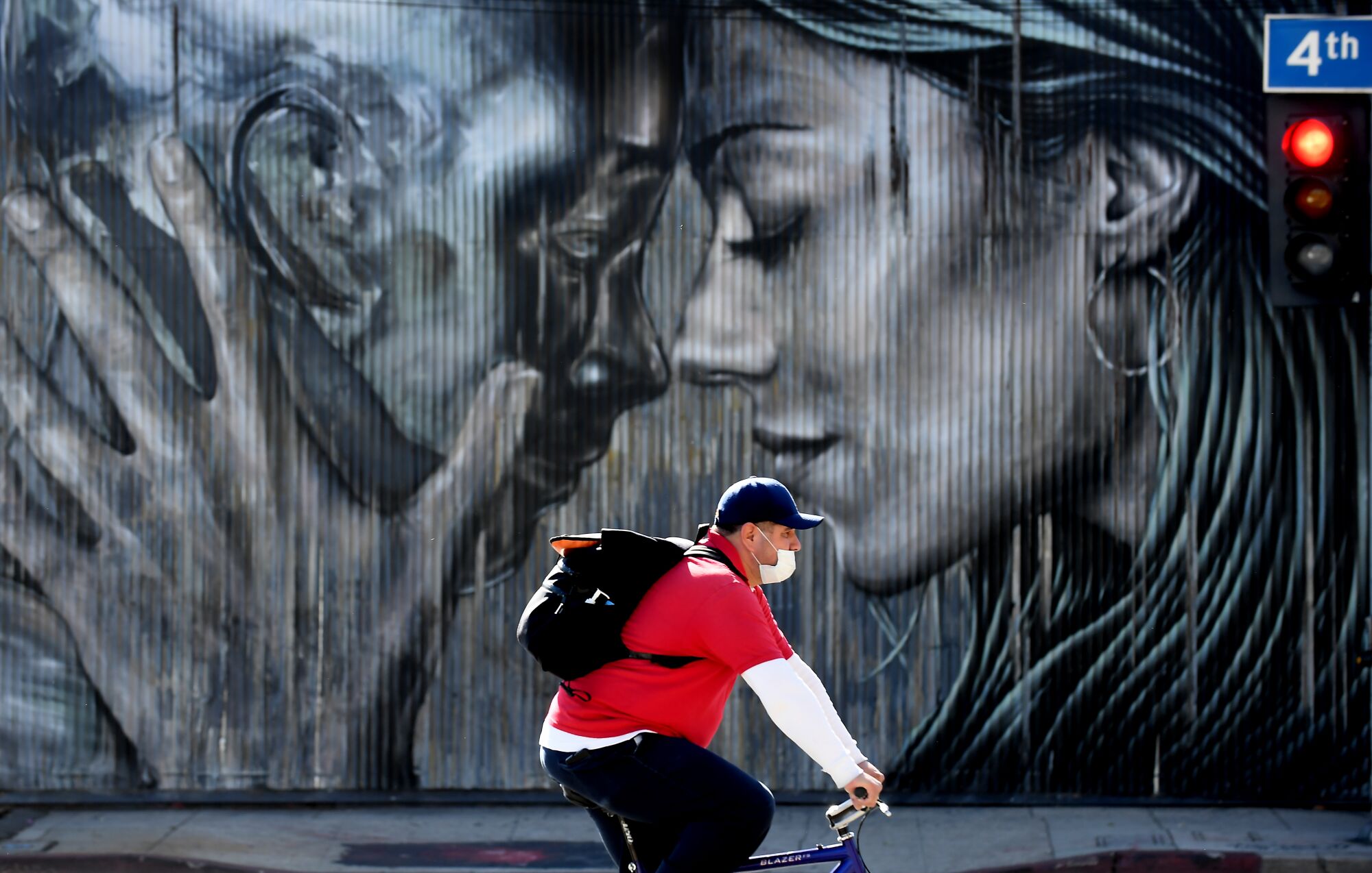 A man rides his bike along 4th Street in Los Angeles with a mural of two people behind him.