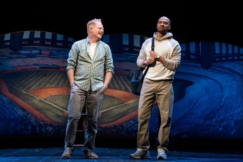 Two male actors talk and smile onstage during a theatrical performance