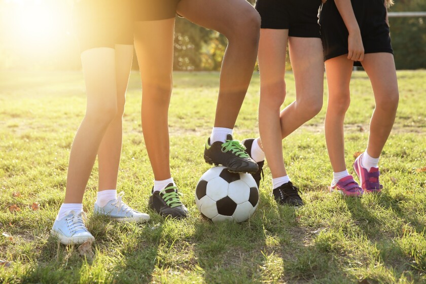 Four girls shown from the waist down, standing with a soccer ball on a field