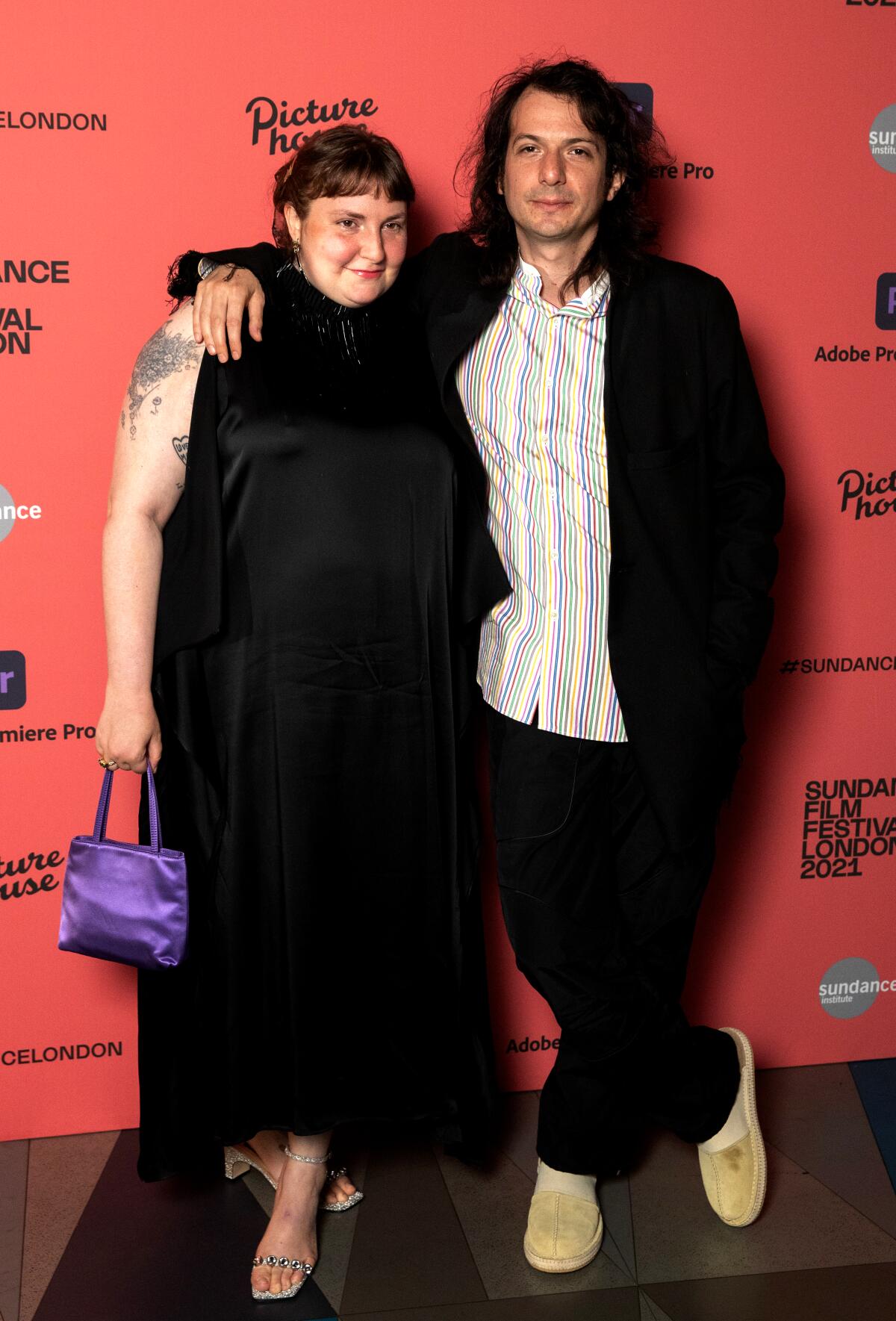 A man stands with his arm around a woman on a red carpet
