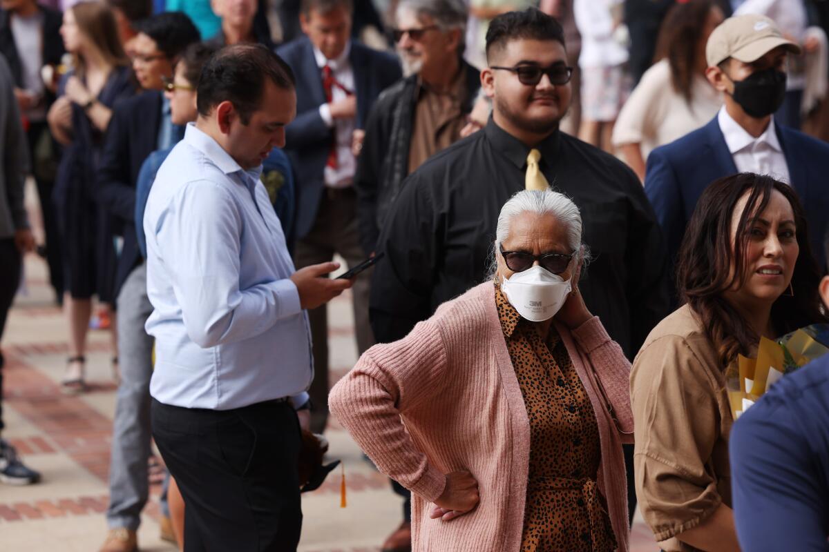 Two people wear protective masks as they stand in a crowd outdoors.