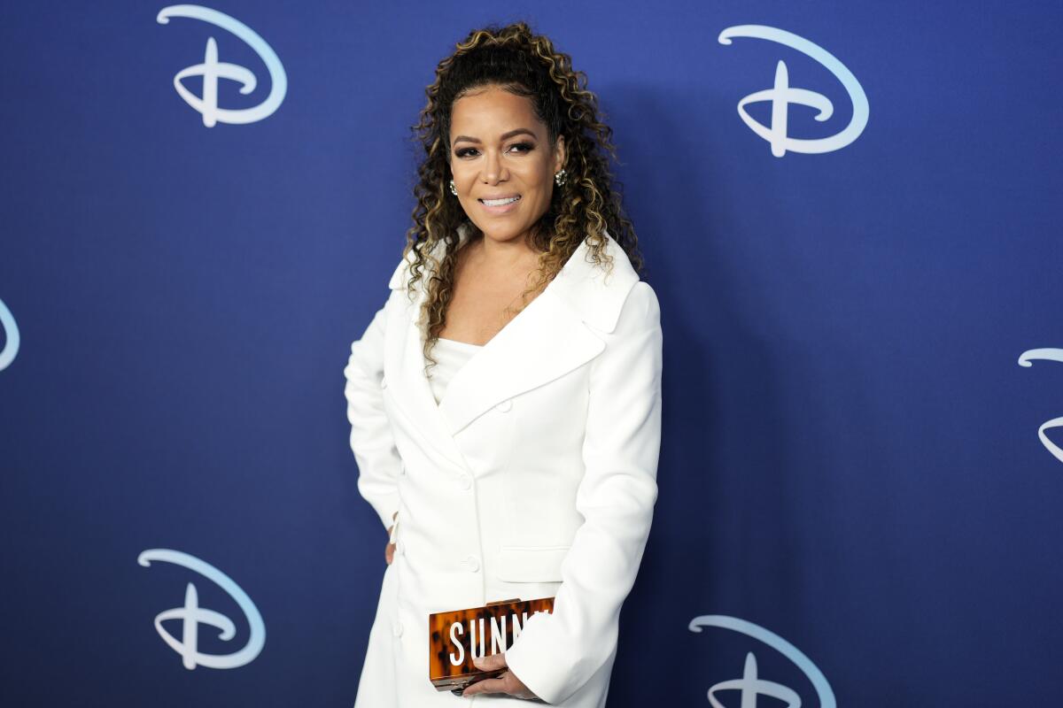 A woman wearing white poses in front of a Disney-branded backdrop