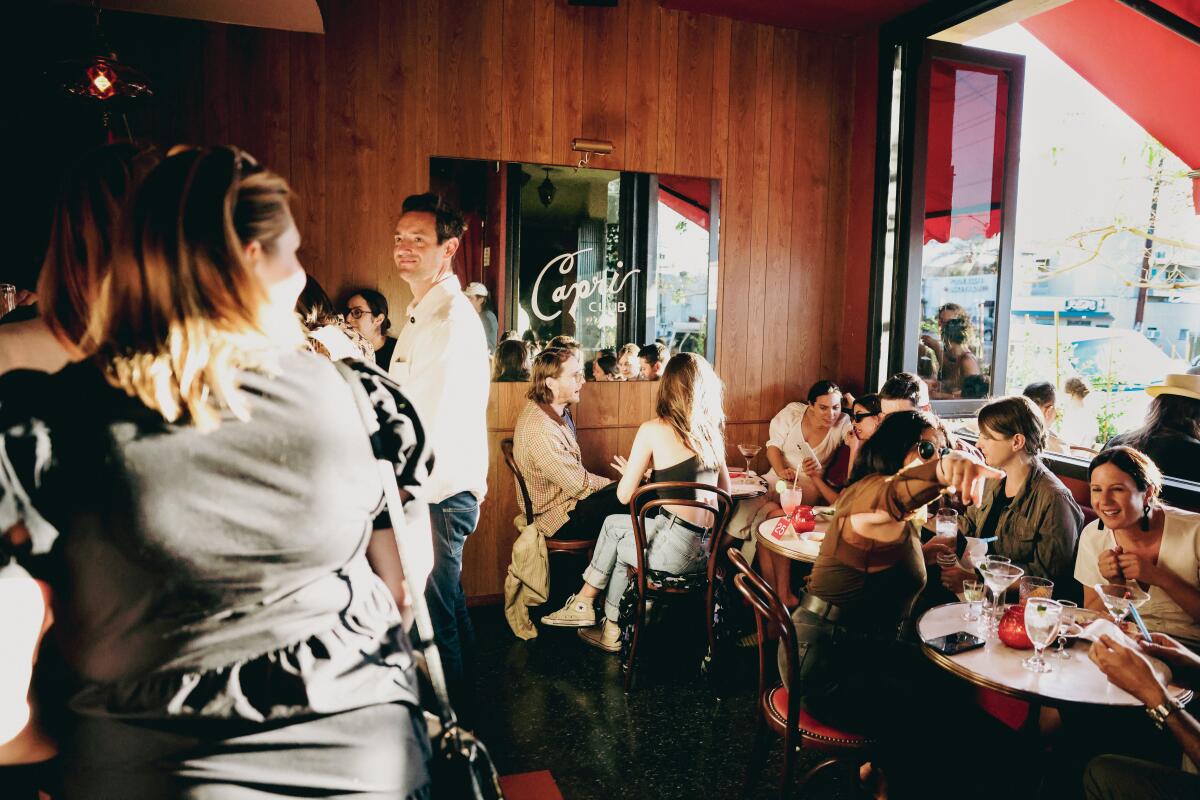 A photo of the interior of the wood-paneled Capri Club, filled with guests at tables and standing at the bar.