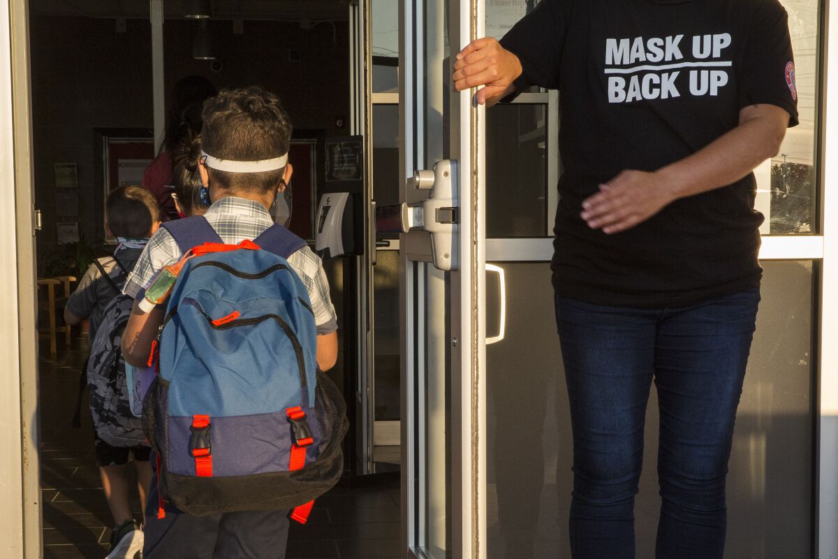 A staff member holds the door open for children on the first day of school in New Braunfels, Texas.