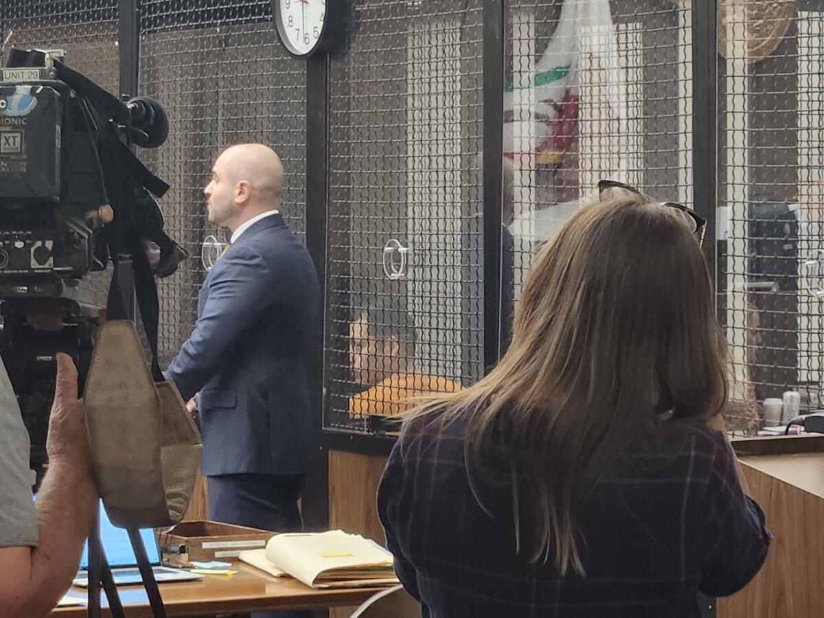 A man in an orange jumpsuit sits in a courtroom.