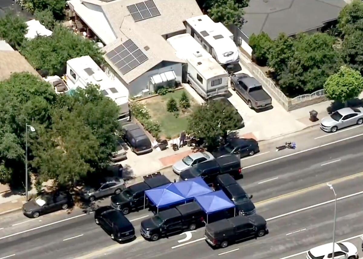An aerial frame of a house and its driveway with a couple of RVs parked in it. Large, black SUVs are blocking the street