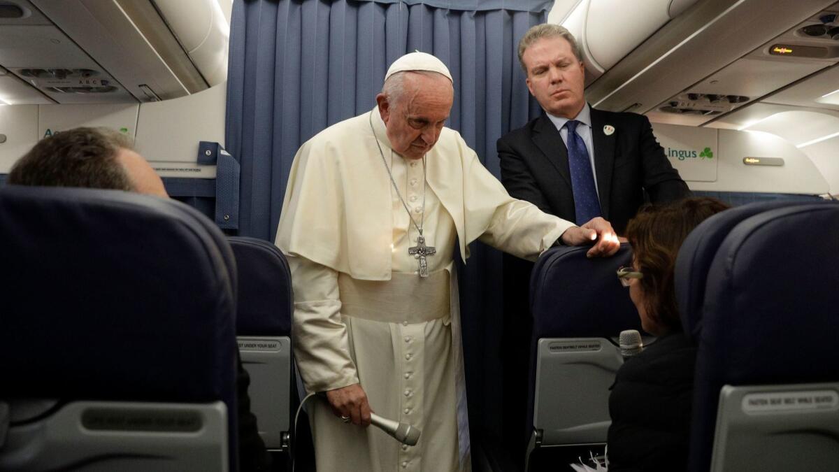Pope Francis, with head of the Vatican press office Greg Burke, addresses a reporter during a news conference Aug. 26 while returning from Ireland to the Vatican at the end of his two-day visit.