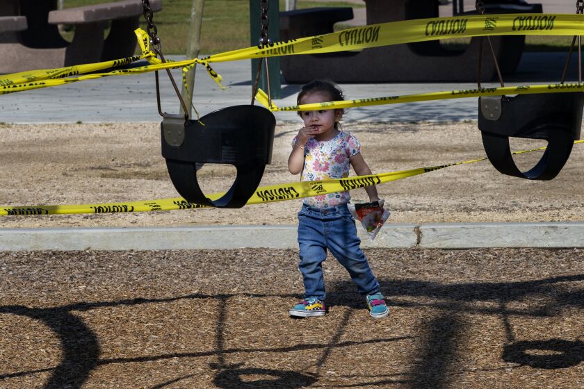 RIVERSIDE, CALIFORNIA - APRIL 3, 2020: Adeline Hernandez, 2, of Riverside seems perplexed by the yellow caution tape as she approaches the closed off swing sets during the coronavirus pandemic at Ryan Bonaminio Park on April 3, 2020 in Riverside, California. She was visiting the park with her dad Erick Hernandez. All the playground equipment and drinking fountains are closed off with yellow caution tape.(Gina Ferazzi/Los Angeles Times)