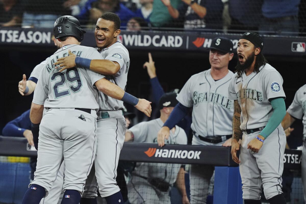 Seattle's Cal Raleigh (29) is greeted by Julio Rodriguez after scoring on Adam Frazier's ninth-inning double.