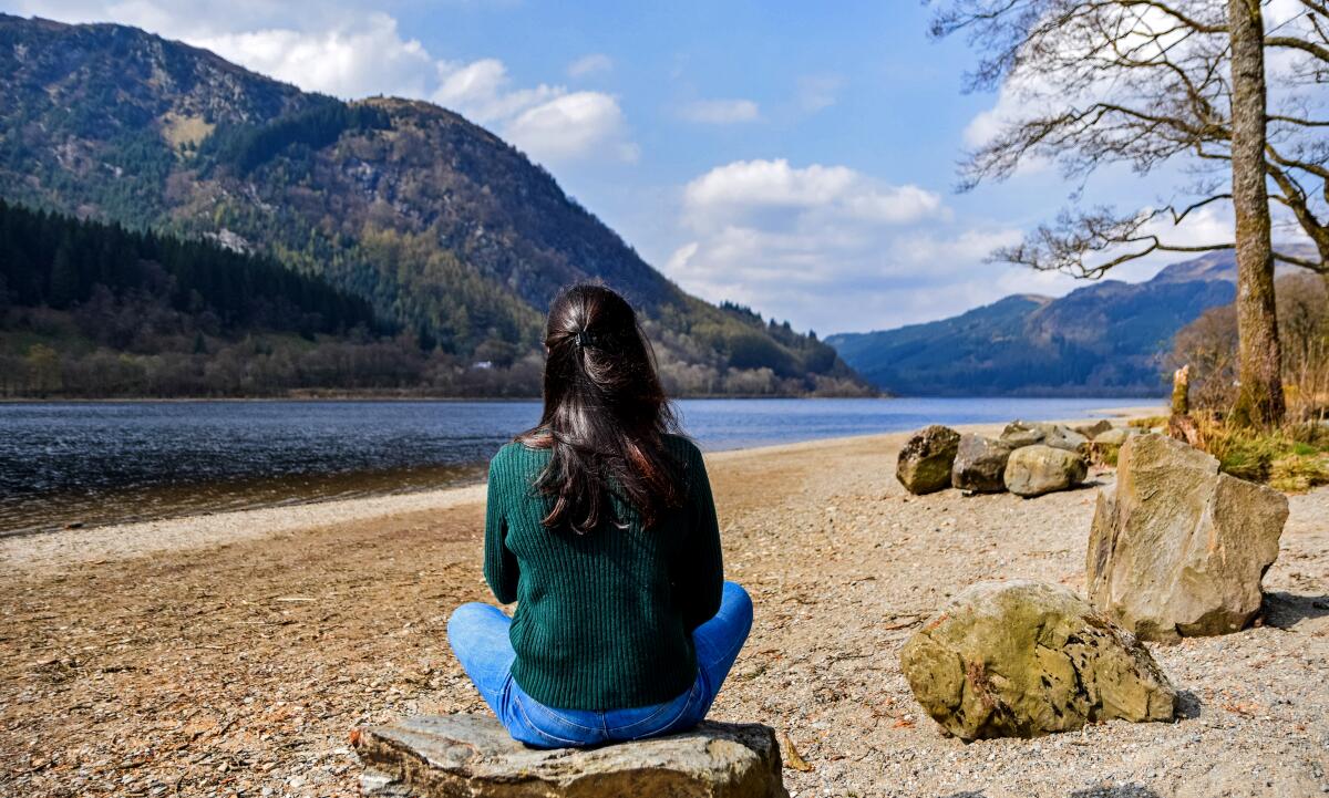 View from behind of a woman sitting on a rock looking at a lake