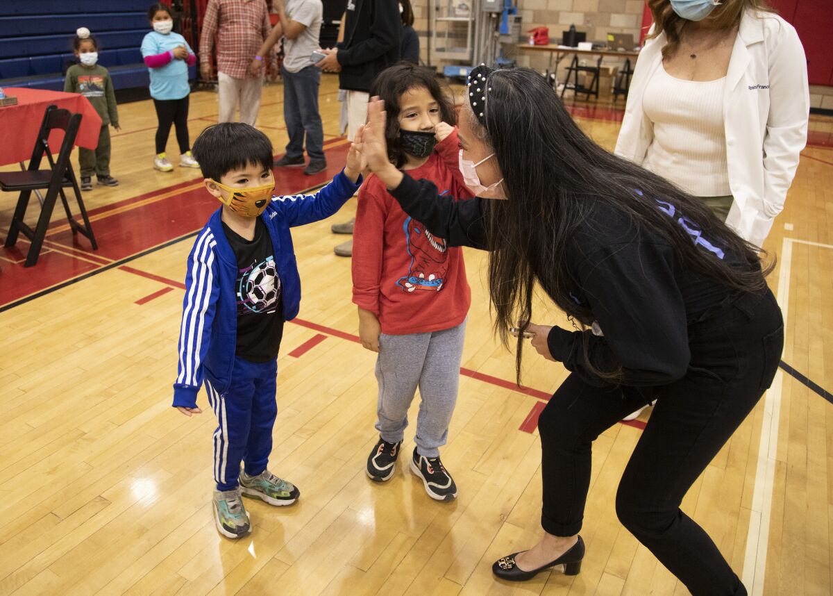 A mother high-fives her son in a school gymnasium with both wearing masks.