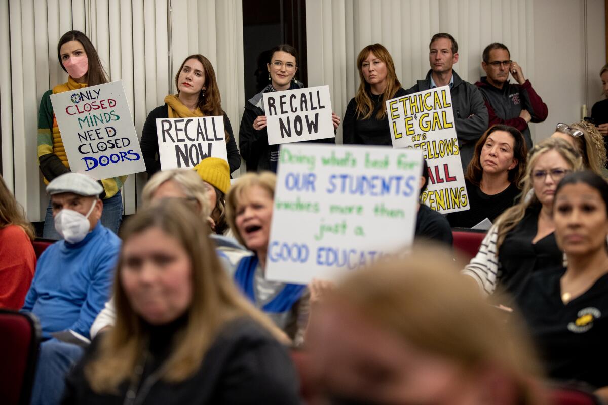 Parents hold signs reading "Recall Now" and "Only Closed Minds Need Closed Doors."