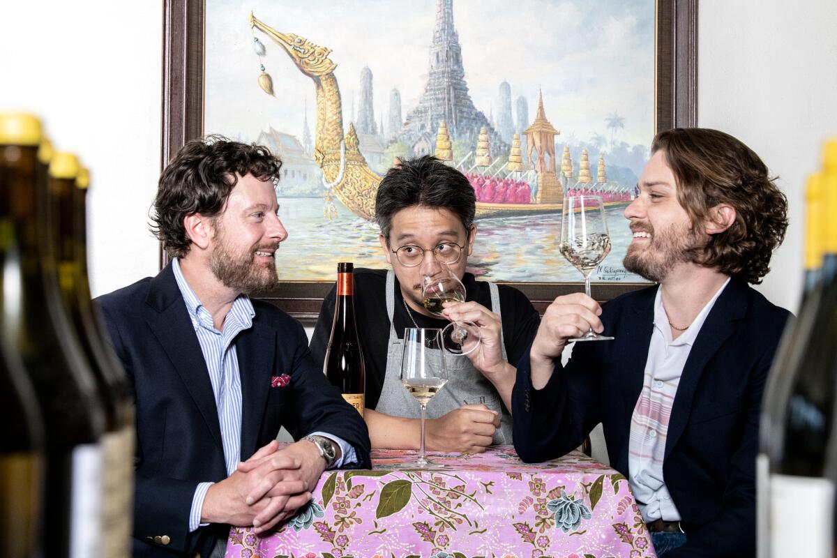 Three people seated at a restaurant table, tasting wine