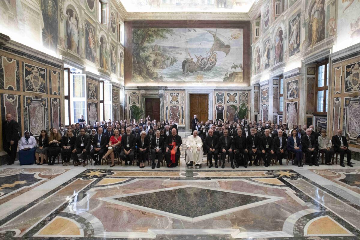 Pope Francis sits with attendees of an international conference in an ornate room.