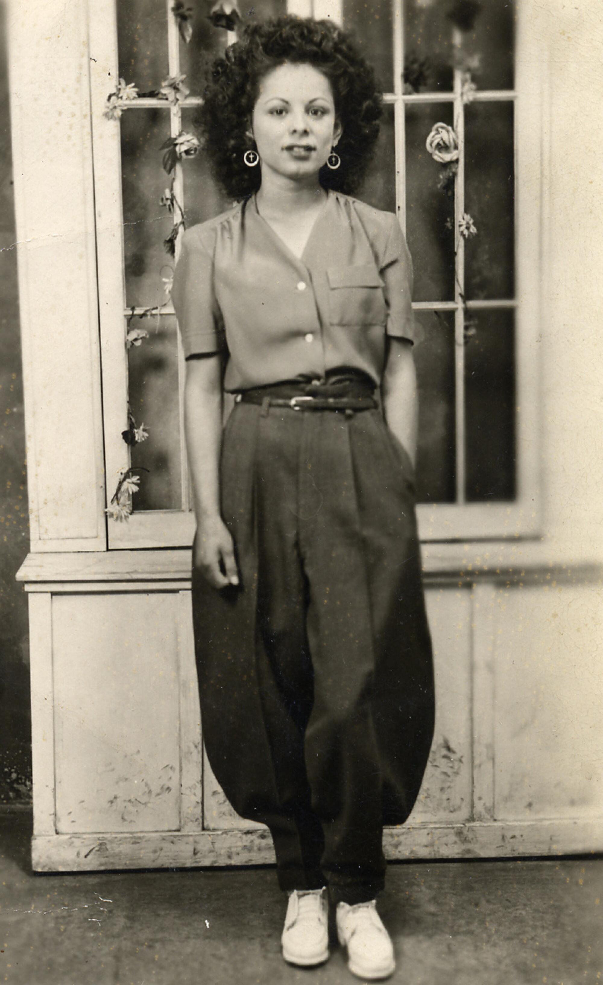 A historic photo shows a woman wearing 1940s drape pants that flare at the knee with a button-down blouse. 