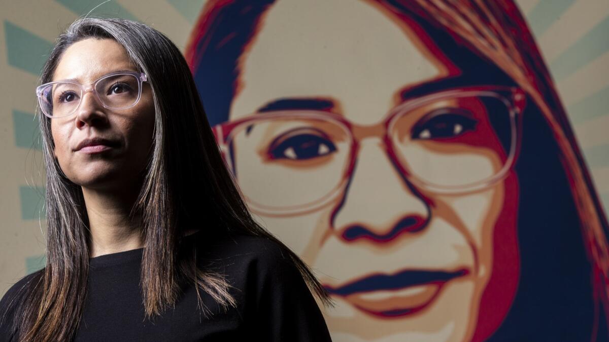Roxana Dueñas' stands before a large version of the poster that features her face at UTLA headquarters.