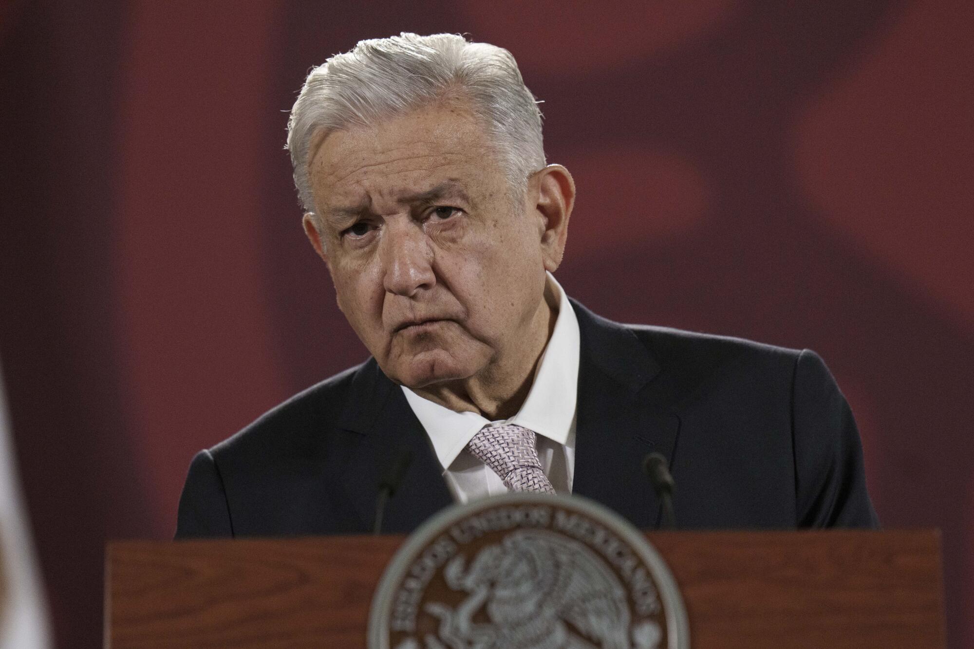 A man with gray hair, in a dark suit, looks out from a lectern 