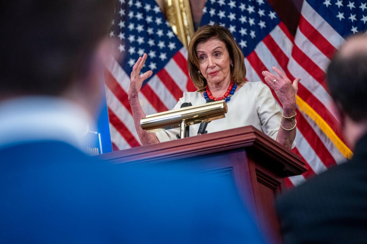 Nancy Pelosi, with flags behind her, gestures as she speaks at a lectern