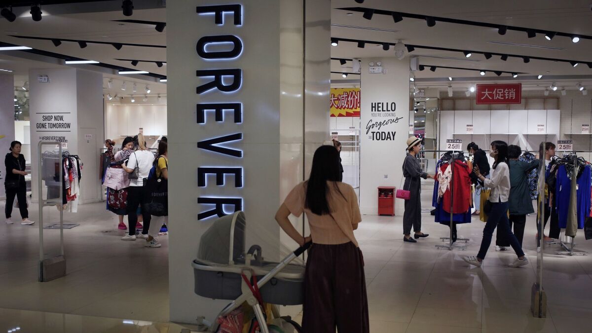 A woman watches as shoppers select clothing at a Forever 21 store in Beijing. The company is pulling out of the China market.