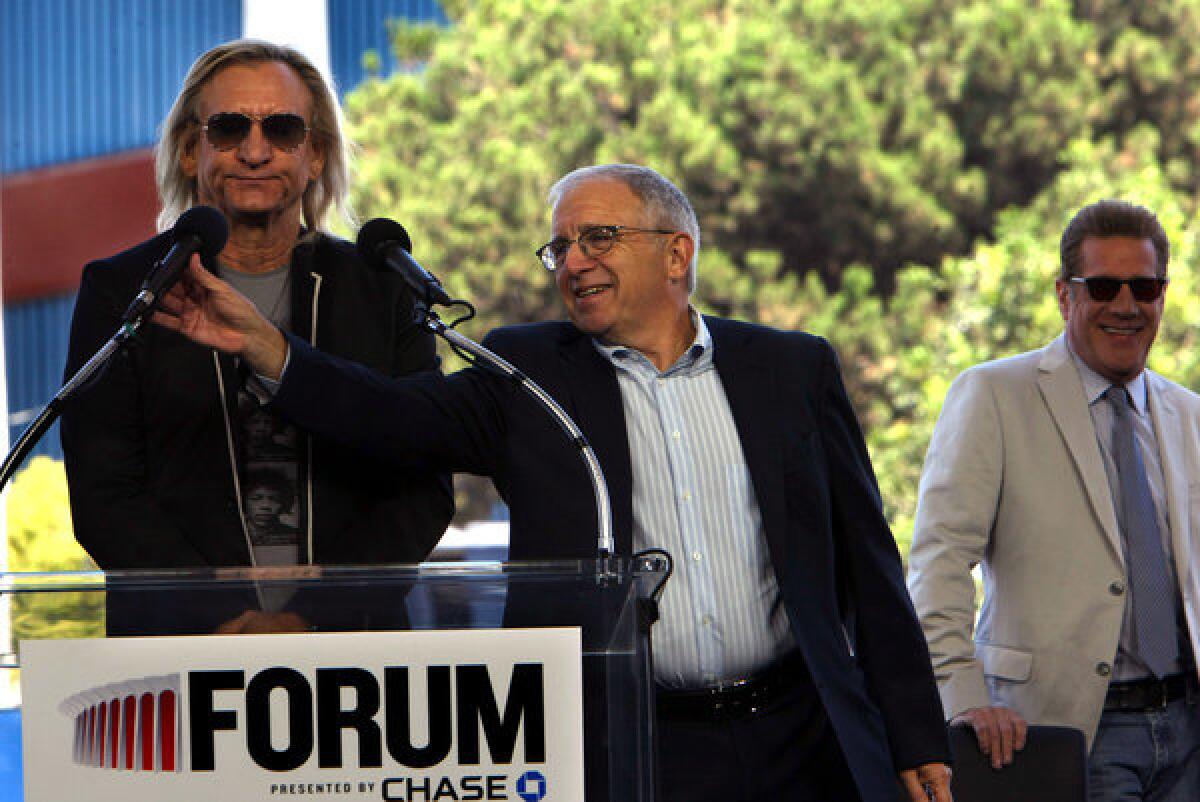 Joe Walsh of The Eagles, left, gets some help with his mike by Irving Azoff, of Azoff Music Management, as Glenn Frey, of The Eagles laughs during a press conference formally unveiling Madison Square Garden's plan to revitalize the Forum in Inglewood.