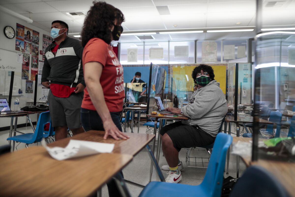High school students wearing masks sit in a classroom. 